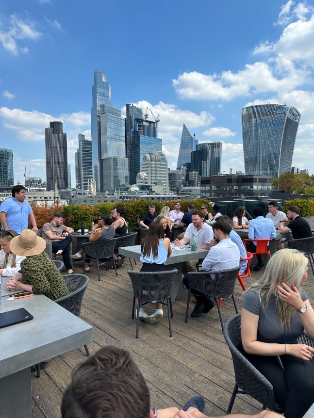 Portrait shot of London high rise skyline, the river and people sat in groups on tables